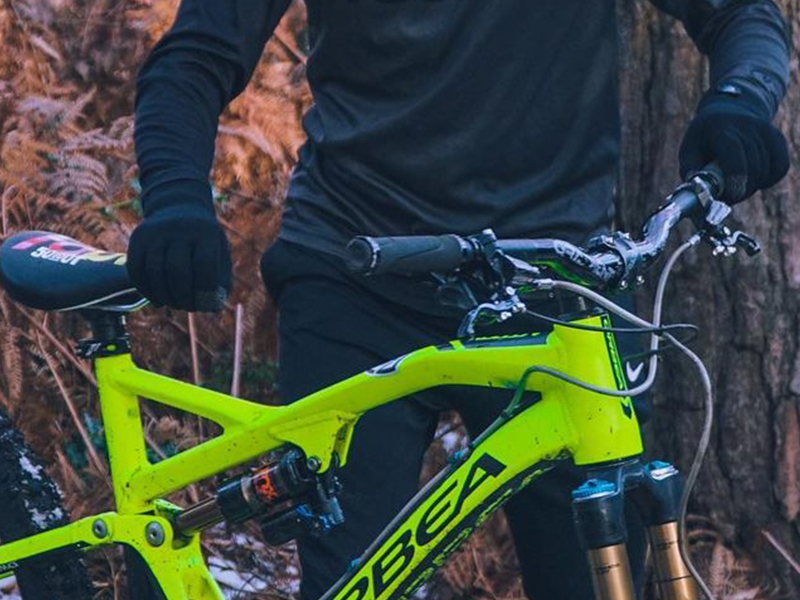 Neon yellow full-suspension mountain bike held by a person in black gear on a forest trail.