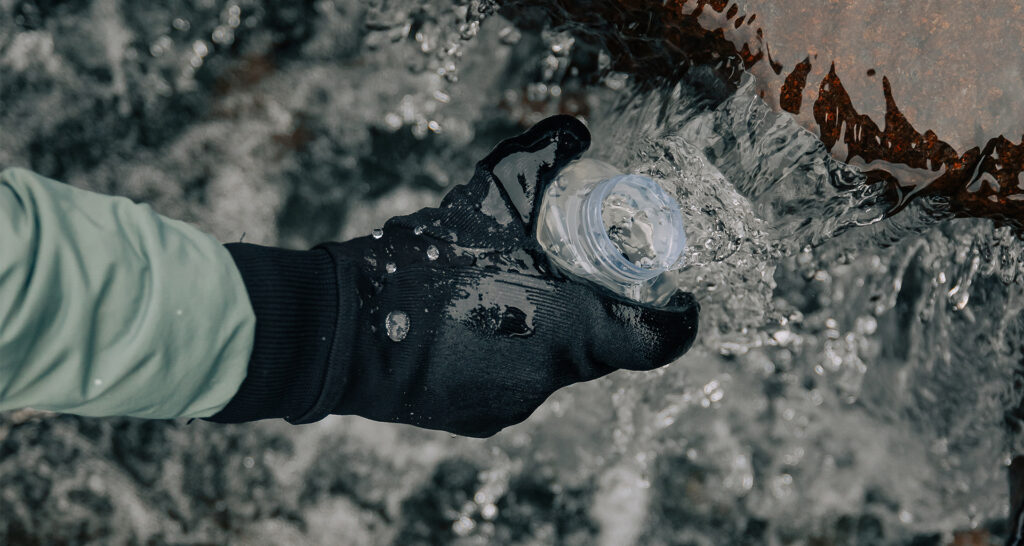 Gloved hand holding a plastic bottle cap under a stream of rushing water.